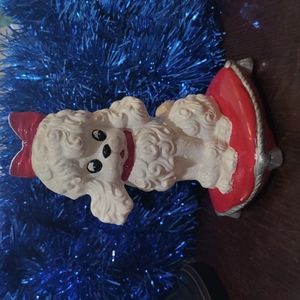 Adorable ceramic white poodle sitting on red pillow